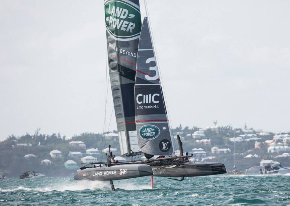 silver racing yacht in the sea with several houses in the background