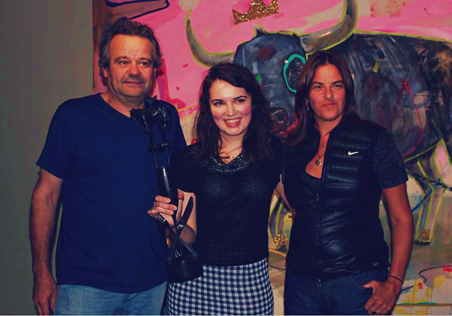 a woman, stood between a man and a woman, holding an award