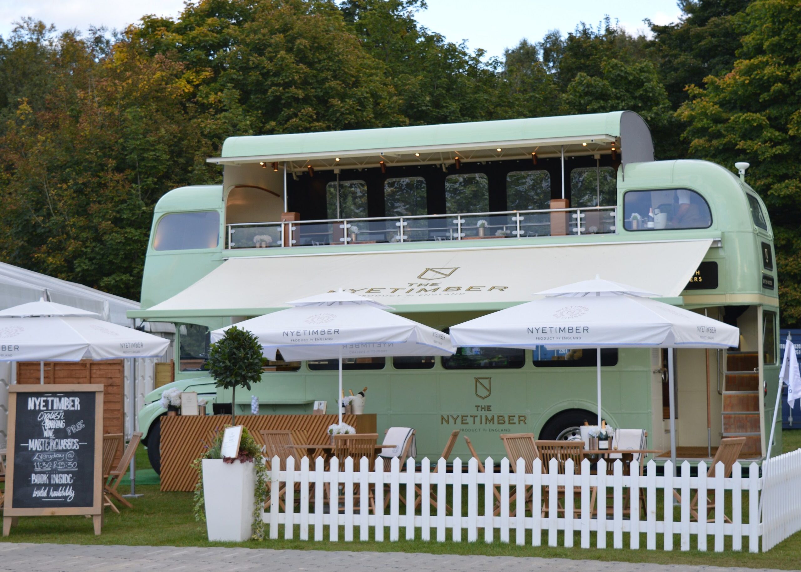 green open top bus set out as a restaurant with tables, chairs and parasols