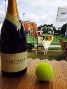 a bottle and glass of wine with a tennis ball, overlooking a tennis match