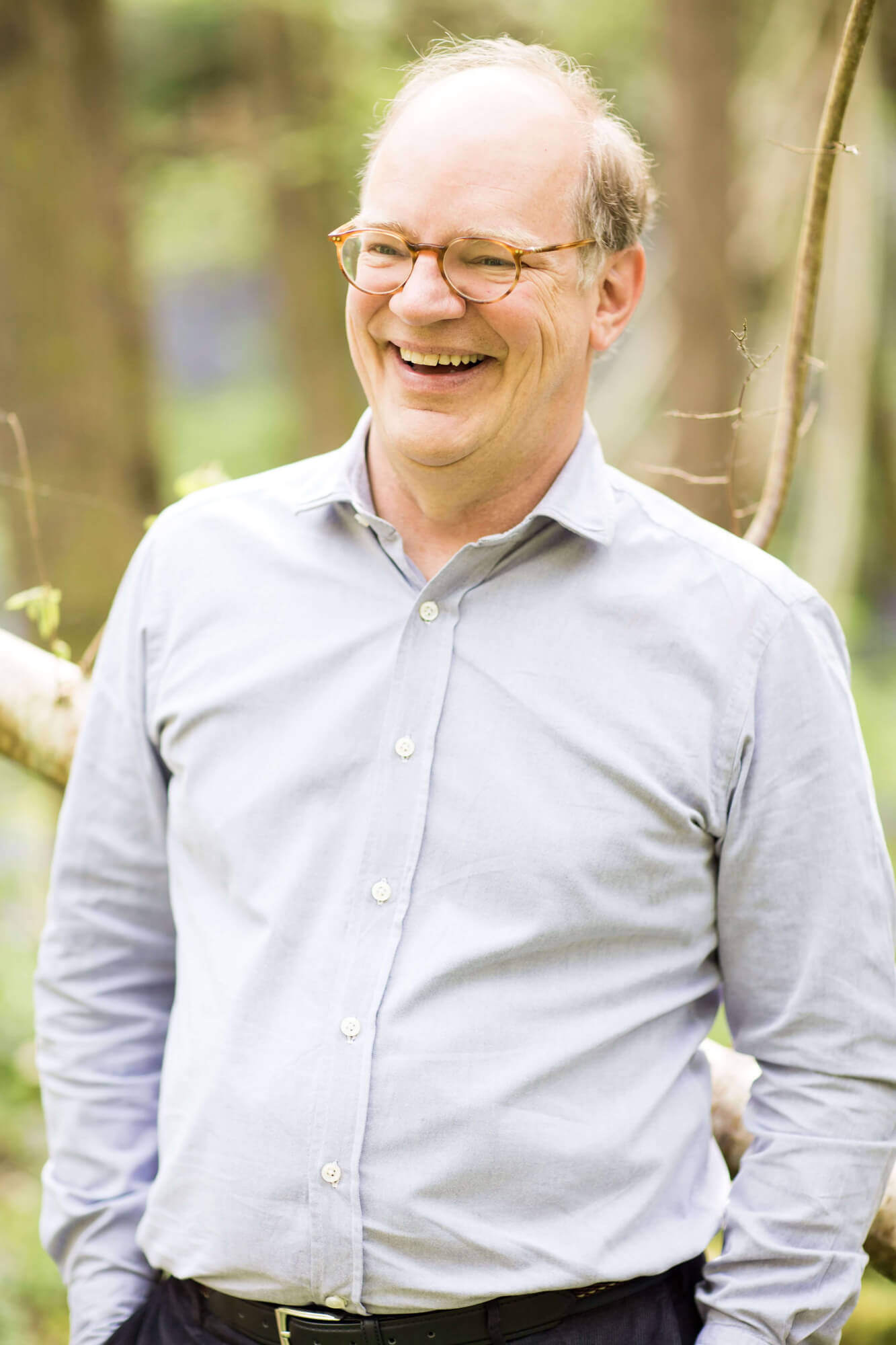 a man with glasses, hands in his pockets, smiling