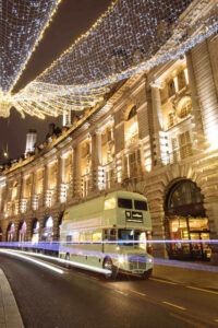 a vintage bus driving through the streets of London at night with lights strung from buildings