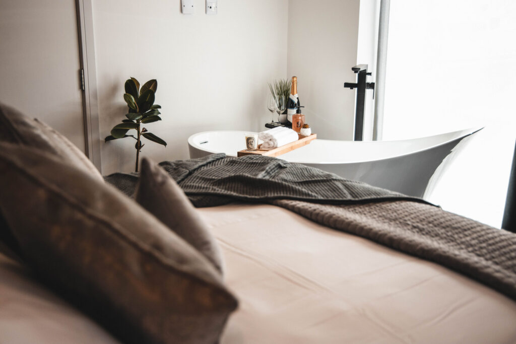 a modern bedroom with a bath and bath tray including Nyetimber Classic Cuvee wine, glasses and candles on the tray