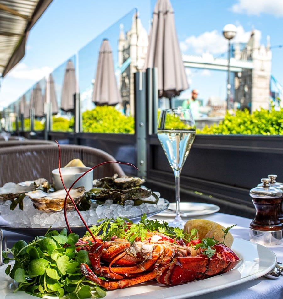 a restaurant table with seafood and a glass of wine that looks onto the Tower Bridge in London